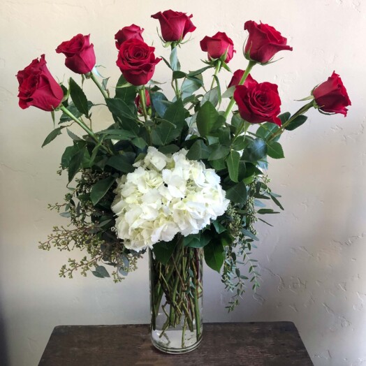 Red roses and hydrangea in tall vase with greens